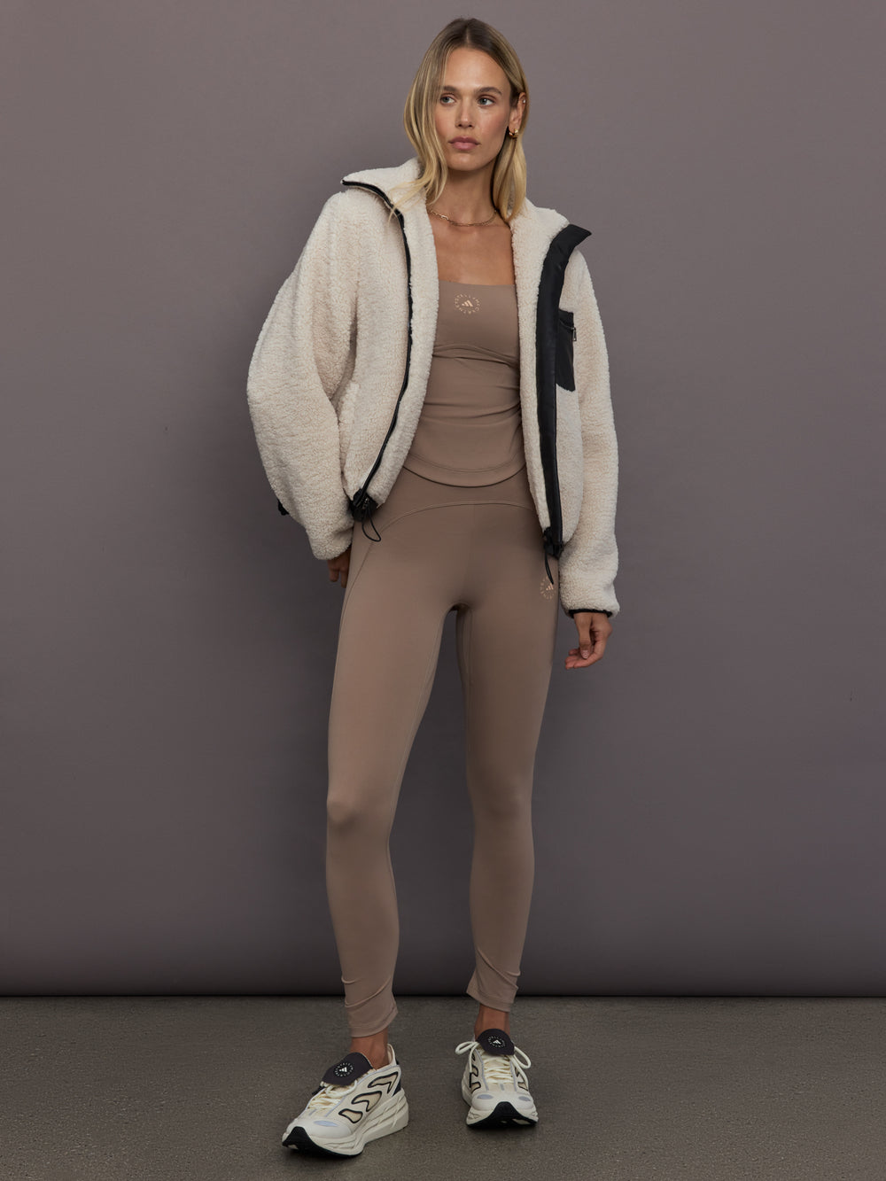 Model is wearing adidas by Stella McCartney Studio Spaghetti Crop Top in Chalky Brown, layered under fleece jacket styling.