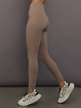 Model is wearing Studio Ruched High-Rise Legging in Chalky Brown, side view.