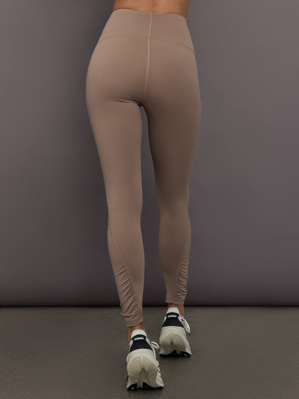Model is wearing Studio Ruched High-Rise Legging in Chalky Brown, back view.