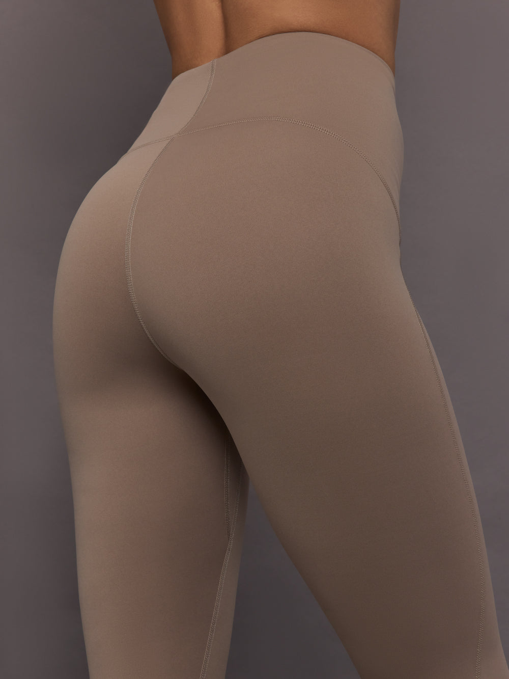 Model is wearing Studio Ruched High-Rise Legging in Chalky Brown, close-up seam detail.