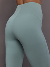 Model is wearing Studio Ruched High-Rise Legging in Wonder Sage, close-up ruched detail.