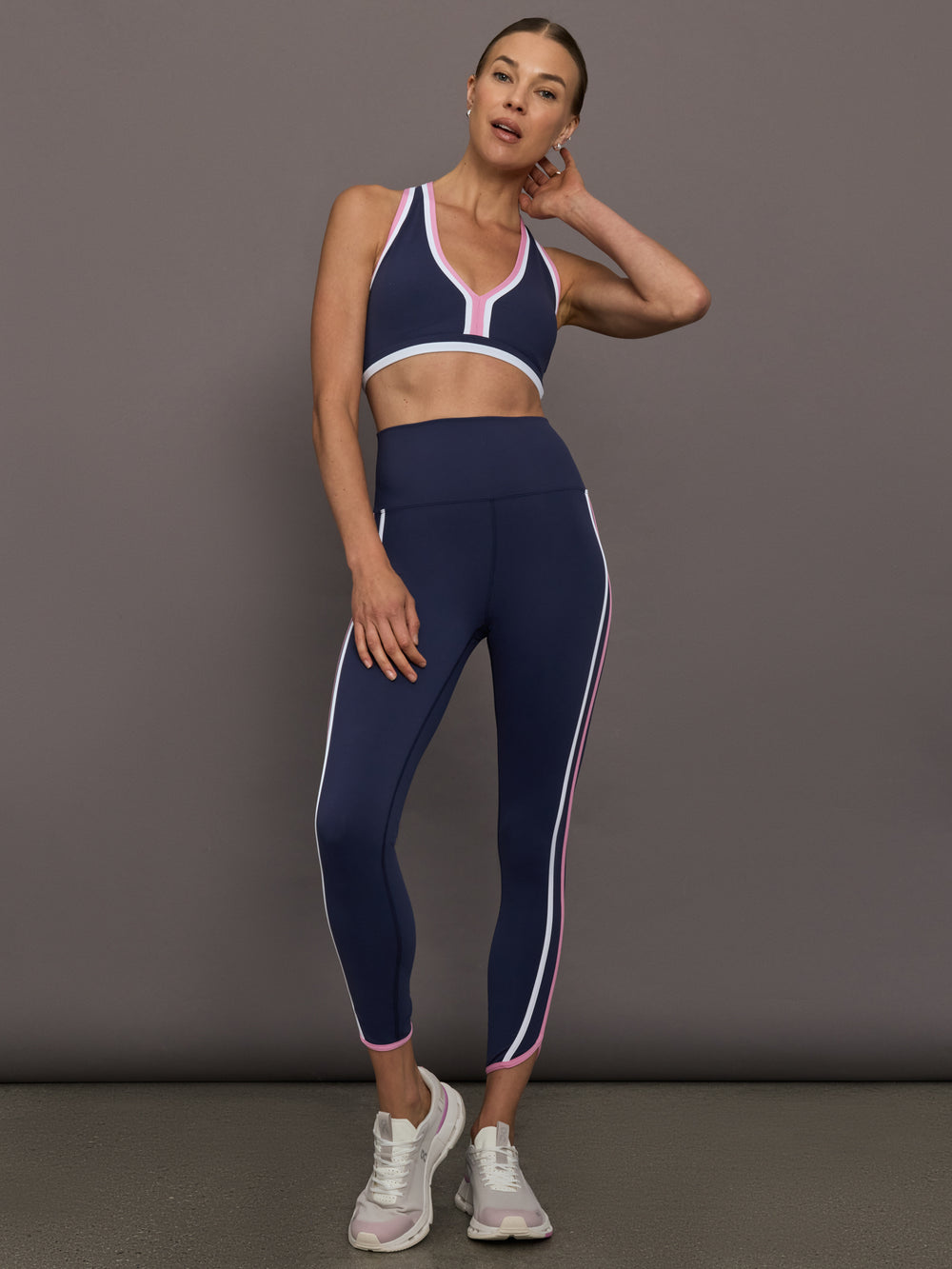 Model wearing Ida Top sports bra and Nella Leggings in navy with pink trim, full body front view.
