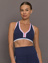 Model wearing Ida Top sports bra in navy with pink and white trim, front view.