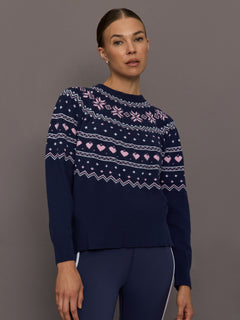 Model wearing navy Fair Isle knit sweater with pink heart and snowflake motifs, front view.