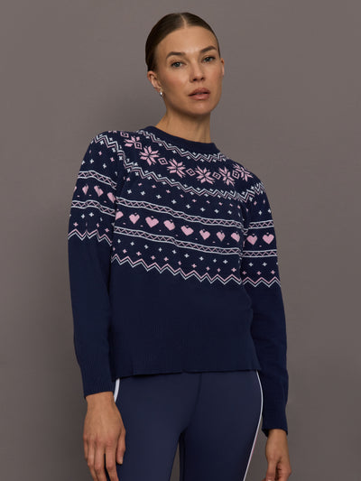 Model wearing navy Fair Isle knit sweater with pink heart and snowflake motifs, front view.