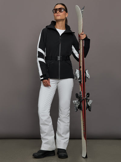 Person in black and white ski outfit holding skis against a gray background