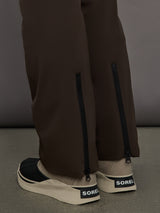 Brown pants with zippers and beige sneakers with SOREL logo on a gray background