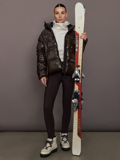 Woman wearing a shiny brown puffer jacket against a gray background