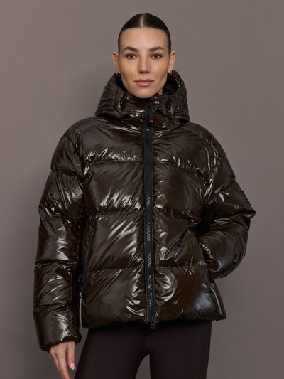 Woman wearing a shiny brown puffer jacket against a gray background