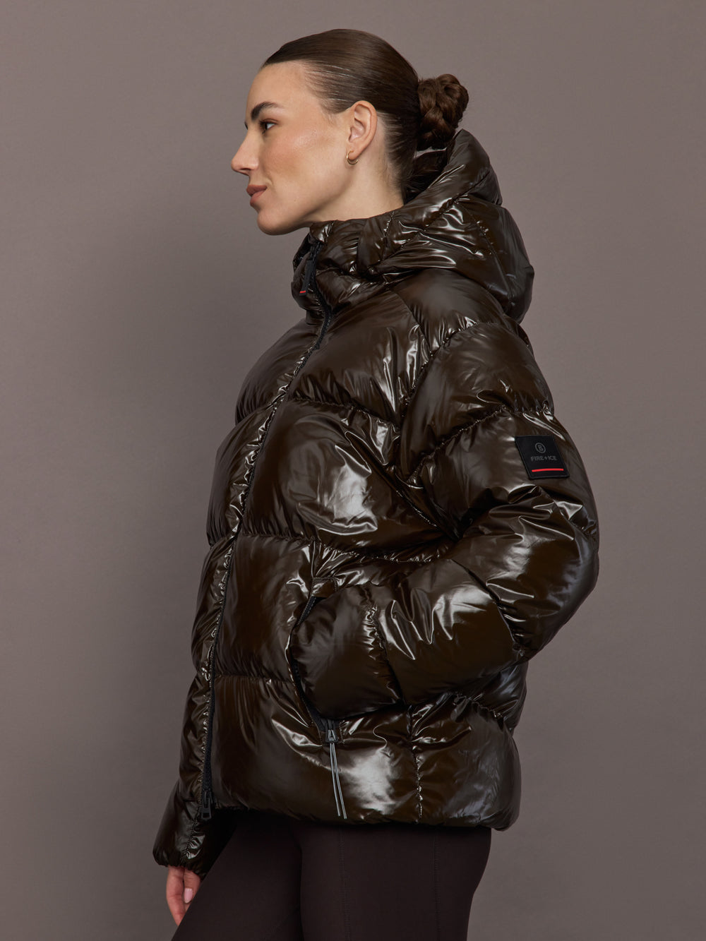 Woman wearing a shiny brown puffer jacket against a gray background