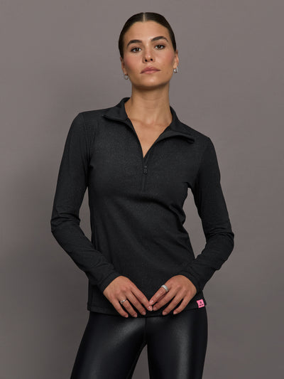 Woman wearing a black long-sleeve top with a quarter zip on a gray background