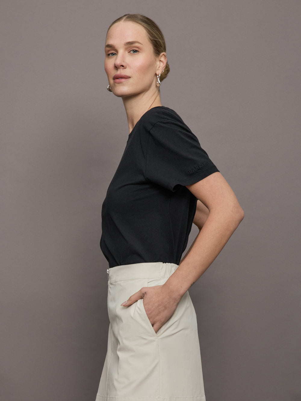 Model wears a basic black tee shirt with ringer neck and the word "Bandier" across the sleeve. 