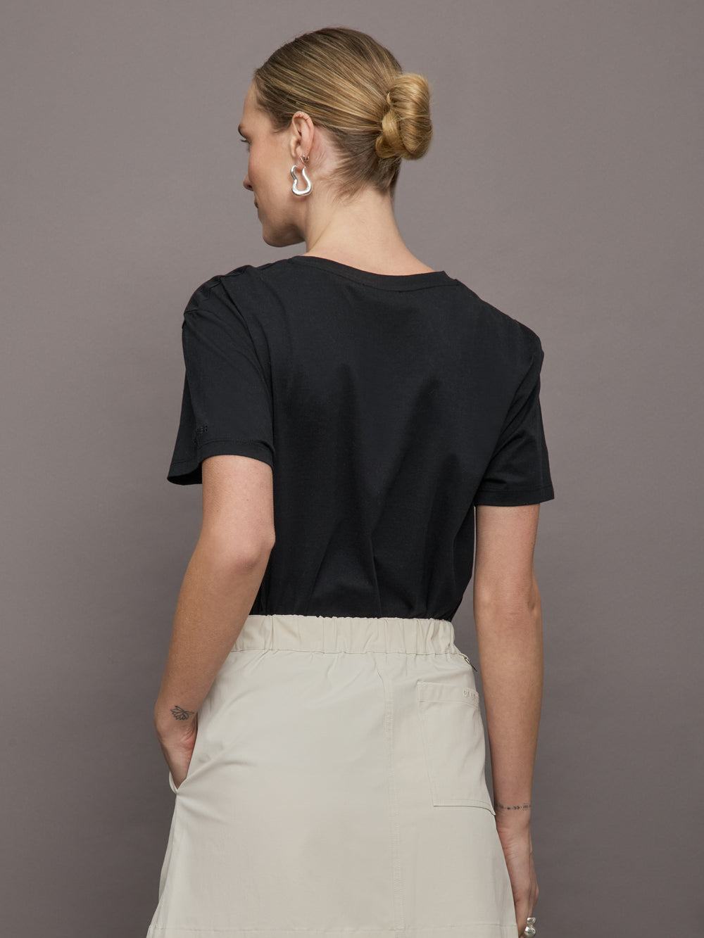 Model wears a basic black tee shirt with ringer neck and the word "Bandier" across the sleeve. 