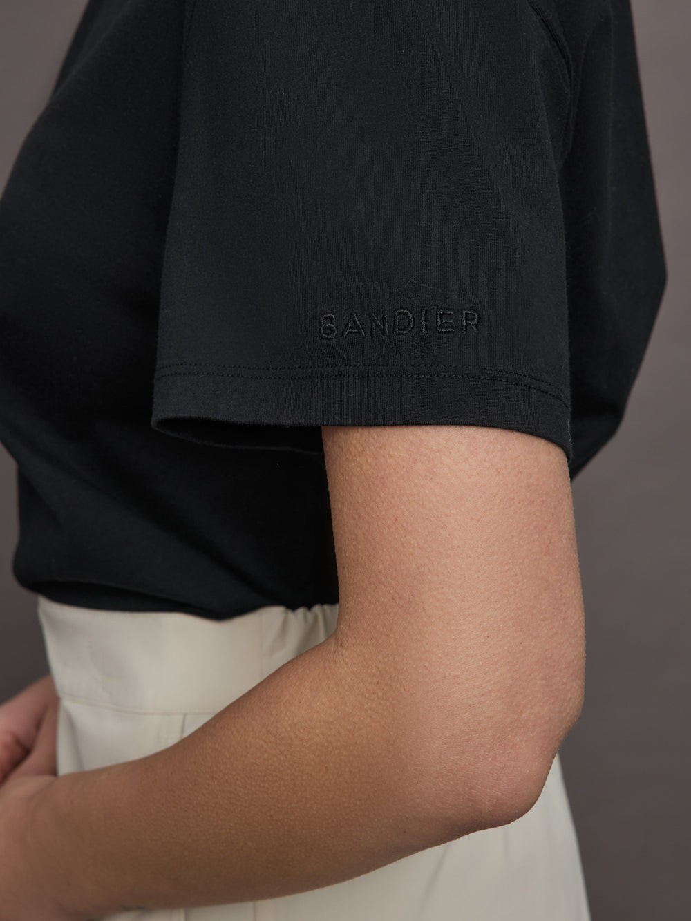Model wears a basic black tee shirt with ringer neck and the word "Bandier" across the sleeve. 