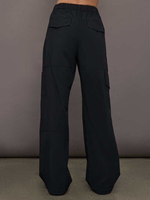 Model wears a pair of black mid-rise wide leg cargo pants with cargo pockets on side, silver zipper in front. 