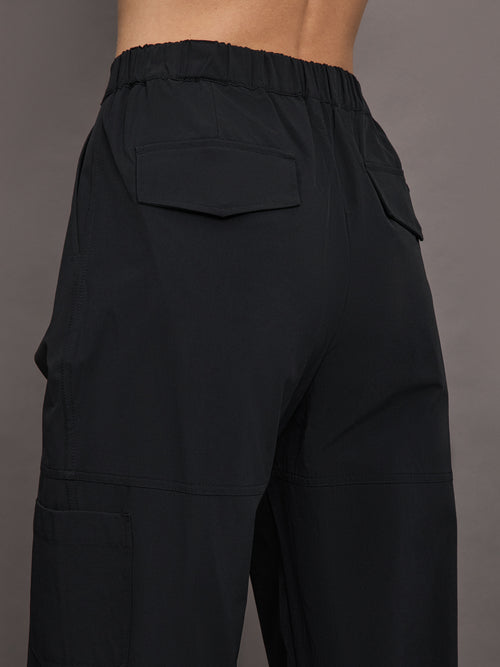 Model wears a pair of black mid-rise wide leg cargo pants with cargo pockets on side, silver zipper in front. 