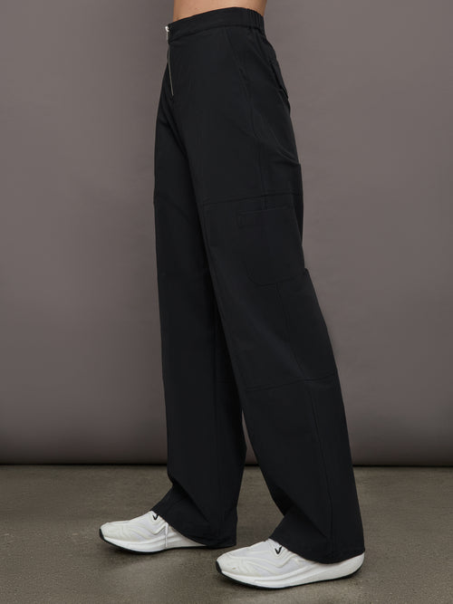 Model wears a pair of black mid-rise wide leg cargo pants with cargo pockets on side, silver zipper in front. 