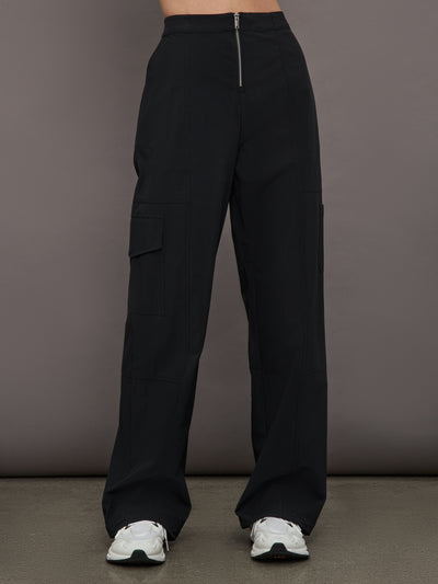 Model wears a pair of black mid-rise wide leg cargo pants with cargo pockets on side, silver zipper in front. 