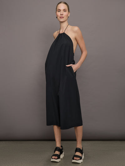 Model wears a loose fitting black dress with haltered neck that hits mid calf. 