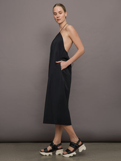 Model wears a loose fitting black dress with haltered neck that hits mid calf. 