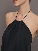 Model wears a loose fitting black dress with haltered neck that hits mid calf. 