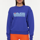 Model wears a royal blue crewneck sweatshirt with the lettering "Soleil Sport" across the chest with wavey lines below and "Bandier" in the bottom right corner. 