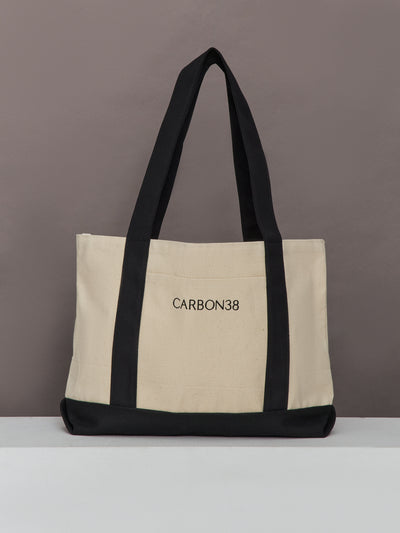 Carbon38 branded tote bag in ivory canvas with black straps and base, front view.