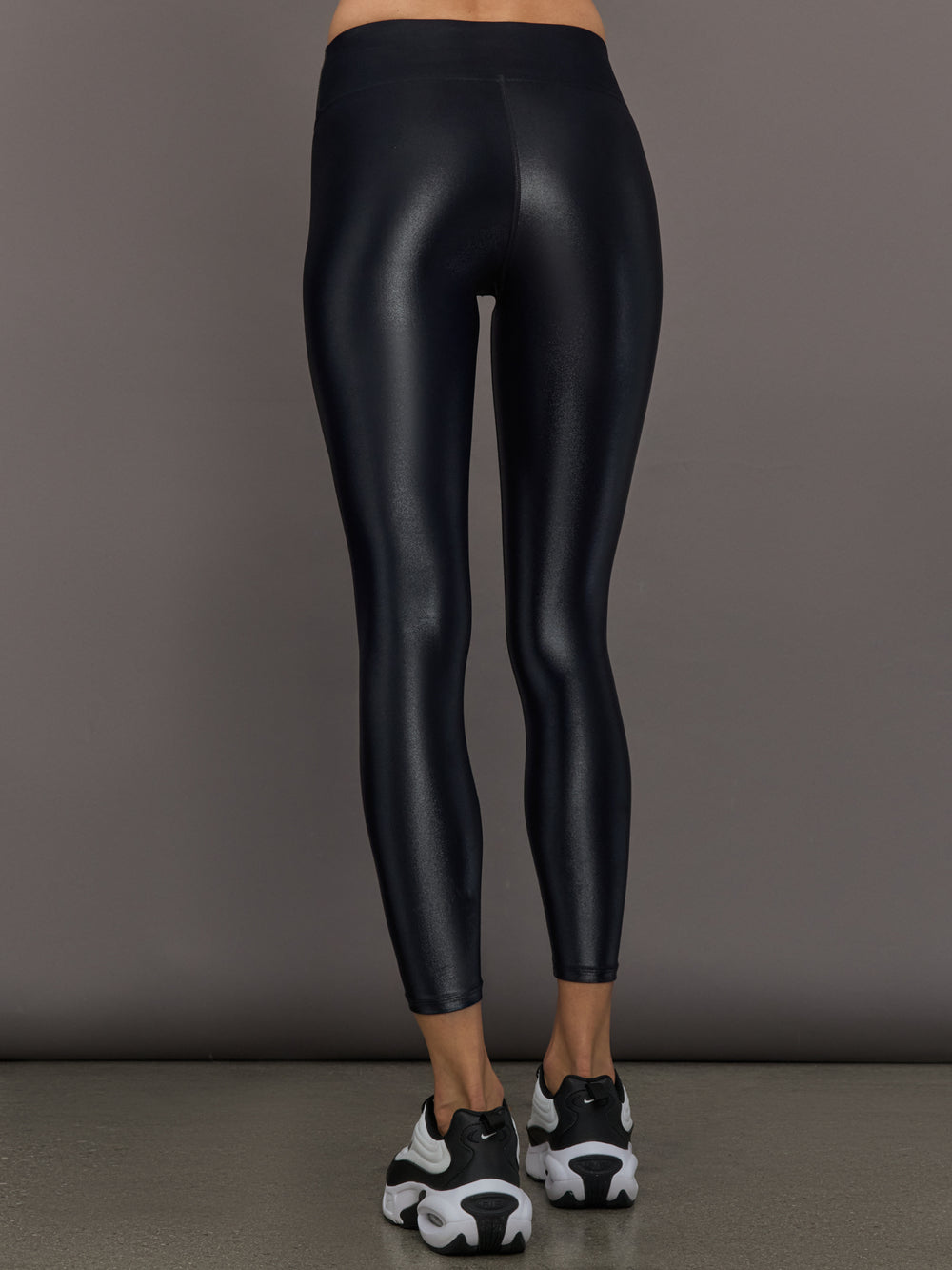 Model wears a mid rise waisted pair of liquidy shine black leggings that hit at model's mid to low calf.
