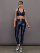 Model is wearing navy mid rise performance leggings in a liquidy-shine finish that hit above the ankle.