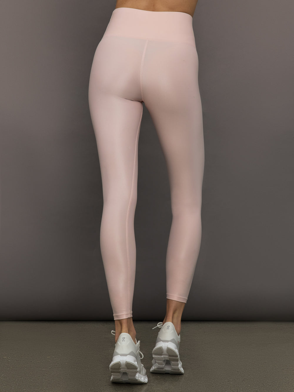 Model wears a pair of high rise baby pink sleek liquidy shine leggings. 