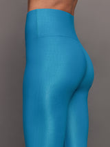 Model wears high rise, liquidy fabrication with crocodile texture, bright blue leggings. 