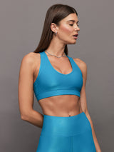 Model wears shiny v neck sports bra with a crocodile texture in a bright blue hue.