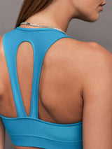 Model wears shiny v neck sports bra with a crocodile texture in a bright blue hue.