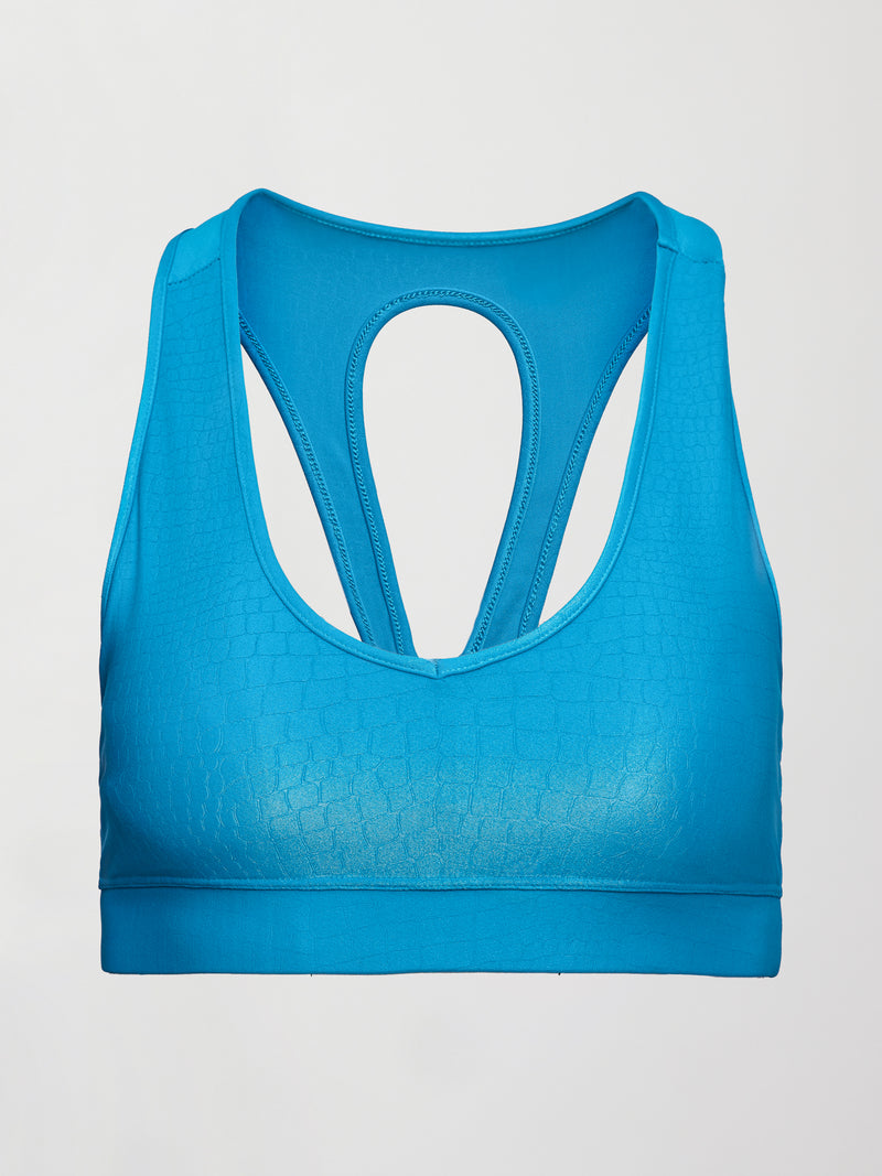 Model wears shiny v neck sports bra with a crocodile texture in a bright blue hue.