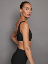 Side profile of ribbed black scoop neck sports bra on model.