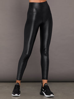 Model wears a high waisted pair of liquidy shine black leggings that hit at model's ankle.