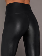 Model wears a high waisted pair of liquidy shine black leggings that hit at model's ankle.