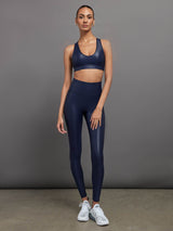 Model is wearing navy high waisted performance leggings in a liquidy-shine finish that hit at the ankle.