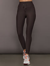 Model is wearing dark brown high-rise leggings with side pockets and adjustable drawstring waistband, full-length fit, front view.