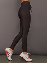 Model is wearing dark brown high-rise leggings with a drawstring waistband and slim side pocket, full-length compression fit, side view.