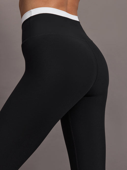 Model wears black full-length leggings with a high-rise, wide waistband with a contrasting white.