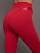 Model wears a sleek, high waisted bright red legging with shiny contoured hip detailing lines. 