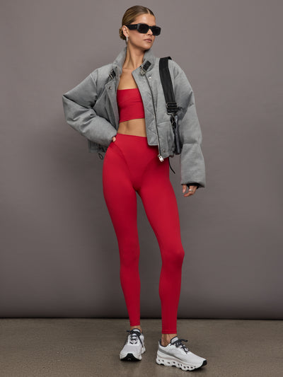 Model wears a sleek, high waisted bright red legging with shiny contoured hip detailing lines. 