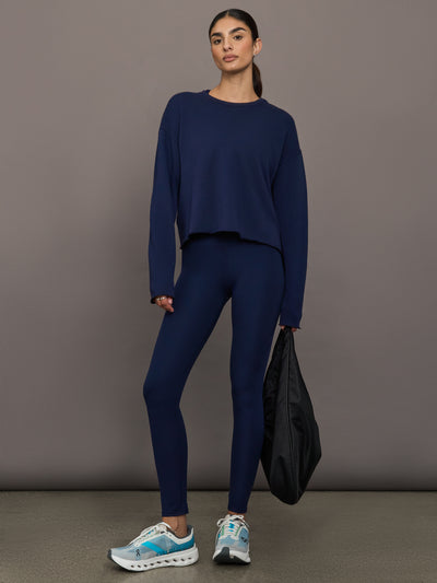 Woman wearing a navy blue outfit holding a black bag against a gray background