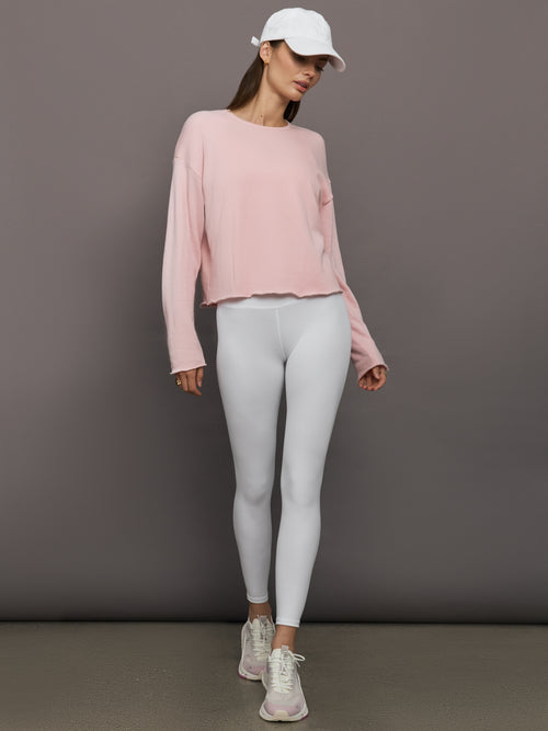 Model wearing white ribbed high-rise leggings styled with pink cropped sweatshirt and white cap, full body view.