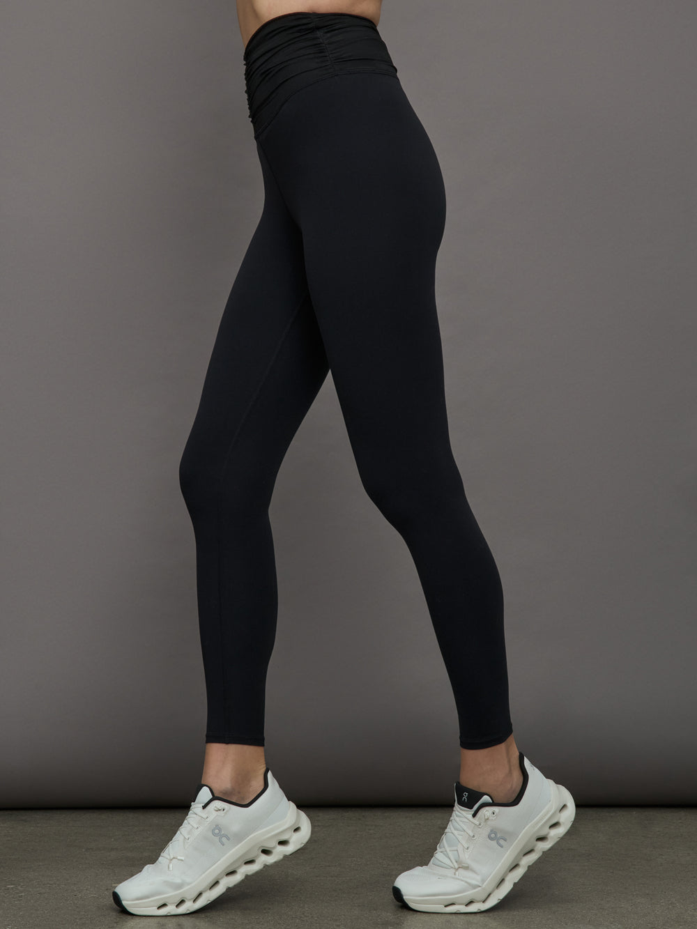 Model wears a pair of high waisted black full length leggings with ruching around the waistline. 