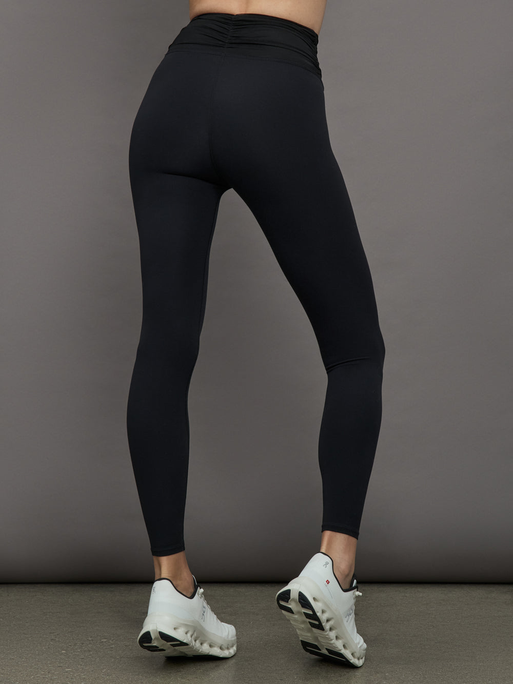 Model wears a pair of high waisted black full length leggings with ruching around the waistline. 