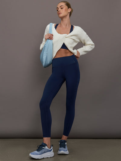 Full body view of model in Diamond Compression High Rise Pocket Legging Navy styled with white cardigan and blue bag.