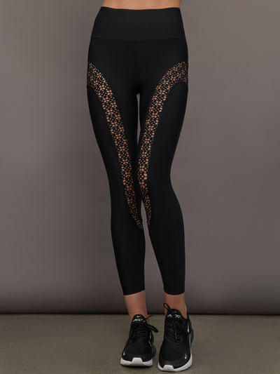 Model wears a pair of black high waisted leggings with laser cutouts along thighs. 