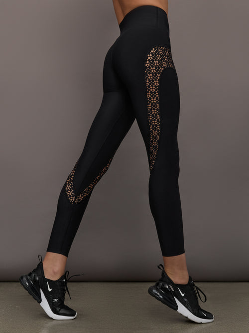 Model wears a pair of black high waisted leggings with laser cutouts along thighs. 
